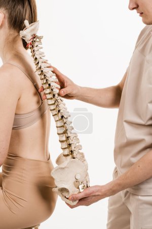 Photo for Scoliosis is sideways curvature of the spine. Backbone anatomical model with young woman. Orthopedist showing spinal column model with girl on white background - Royalty Free Image