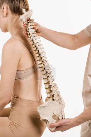 Photo for Scoliosis is sideways curvature of the spine. Backbone anatomical model with young woman. Orthopedist showing spinal column model with girl on white background - Royalty Free Image