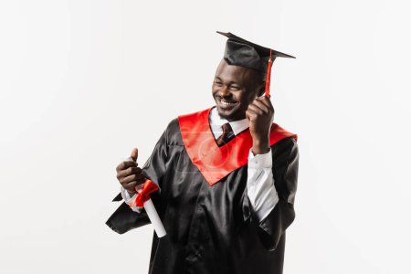 Téléchargez les photos : Diplômé. Heureux homme africain souriant et titulaire d'un diplôme avec les honneurs dans ses mains sur fond blanc. Homme africain diplômé diplômé de l'université et a obtenu un diplôme de maîtrise - en image libre de droit