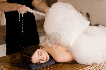 Attractive girl relaxing in spa. Masseur is making foam peeling in Turkish spa hammam