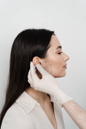 Foto de Cirugía de oreja de otoplastia. Otoplastia remodelación quirúrgica del pabellón auricular y la oreja. Médico cirujano examina las orejas de niña antes de la otoplastia cirugía estética - Imagen libre de derechos