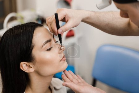 Photo for ENT doctor is drawing mark up lines on nose before rhinoplasty surgery. Rhinoplasty markup. Rhinoplasty is reshaping nose surgery for change appearance of the nose and improve breathing - Royalty Free Image