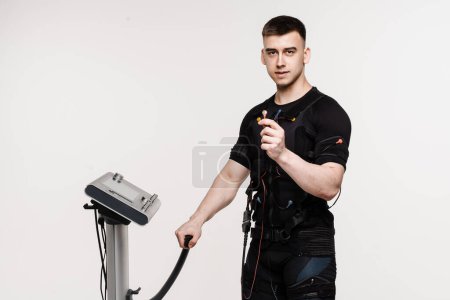 Photo for Muscular male athlete in EMS suit with contactor in hand that uses electrical impulses to stimulate muscles on white background. Sport training in electrical muscle stimulation suit - Royalty Free Image