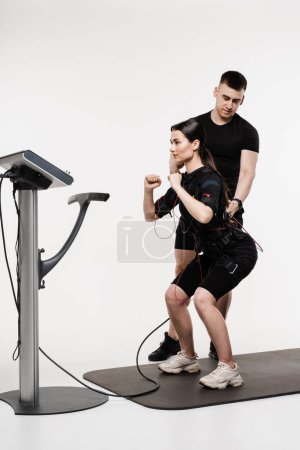 Photo for Group workout training in EMS suit, which applies electrical impulses to activate muscles. Trainer shows an example of the exercise using EMS electrical muscle stimulation suit - Royalty Free Image