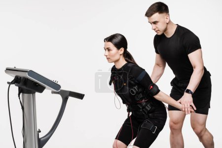 EMS sport training in electrical muscle stimulation suit. Man and girl in EMS suit that uses electrical impulses to stimulate muscles on white background