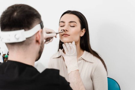 Photo for Consultation with ENT doctor. Otolaryngologist examines girl nose before procedure of endoscopy of nose. Rhinoscopy of woman nose - Royalty Free Image