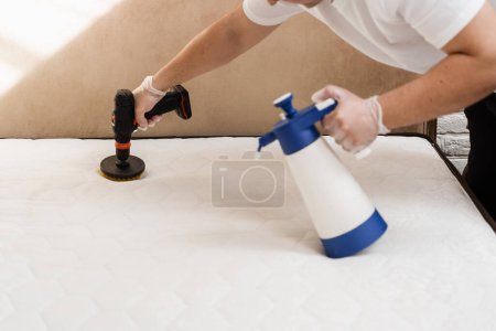 Photo for Spraying and smearing detergent on white mattress using drill with brush for dry cleaning. Applying detergent on mattress for dry cleaning - Royalty Free Image