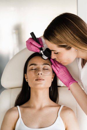 Photo for Dermatologist examines moles and birthmarks of girl patient using dermatoscope. Dermatoscopy of skin lesions and moles with dermatoscope for preventing skin cancer and melanoma - Royalty Free Image