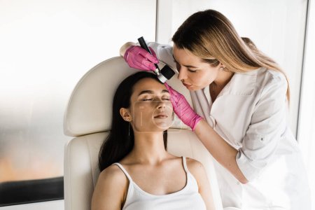 Photo for Dermatoscopy of skin lesions and moles with dermatoscope for preventing skin cancer and melanoma. Dermatologist examines moles and birthmarks of girl patient using dermatoscope - Royalty Free Image