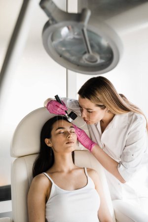 Photo for Dermatoscopy of skin lesions and moles with dermatoscope for preventing skin cancer and melanoma. Dermatologist examines moles and birthmarks of girl patient using dermatoscope - Royalty Free Image
