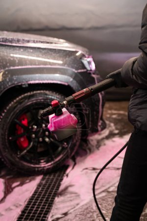 Pistola de espuma con detergente rosa en el fondo del coche. El proceso de lavado de automóviles con equipos especiales y detergentes