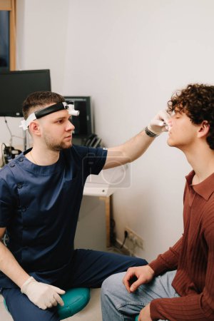 Rhinoscopy medical examination at a private ENT clinic before rhinoplasty or septoplasty surgery. ENT doctor checking nose of man patient with rhinoscope