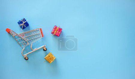 Foto de Carrito de compras con cajas de regalo sobre fondo azul - Imagen libre de derechos
