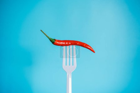 Foto de Un pimiento rojo con un tenedor sobre un fondo azul. el concepto de alimentación saludable. - Imagen libre de derechos