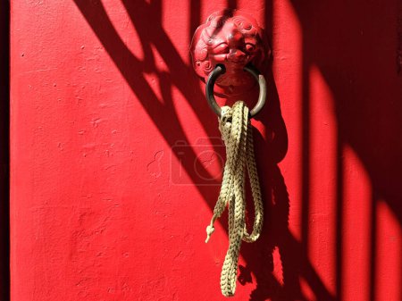 Foto de Anillo golpeador de león vintage en puerta de madera roja con haz de luz y sombra. - Imagen libre de derechos