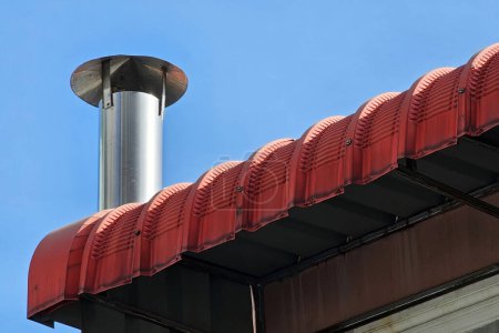 Téléchargez les photos : Cheminée en acier inoxydable sur le toit rouge avec fond bleu ciel. - en image libre de droit