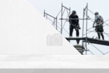 Foto de Mesa Loft mínima con pared de hormigón blanco y dos trabajadores borrosos en el fondo del sitio de construcción con fugas de luz, adecuado para el fondo de la presentación del producto, pantalla y simulacro. - Imagen libre de derechos
