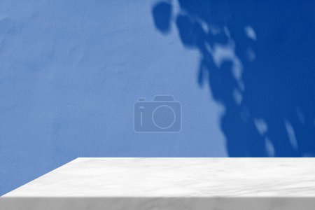 Foto de Esquina de mesa de mármol blanco con haz de luz, sombra y foco en el fondo de pared de hormigón azul, adecuado para el fondo de la presentación del producto, pantalla y simulacro. - Imagen libre de derechos