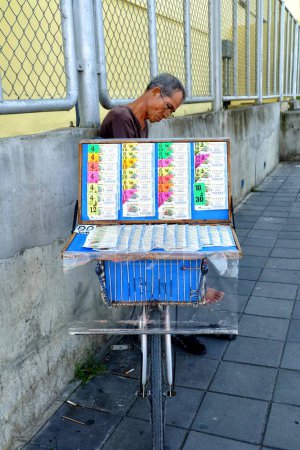 Foto de BANGKOK, TAILANDIA - 28 DE JUNIO DE 2017: Vendedor de billetes de lotería no identificado Sentado en Bangkok, Tailandia. - Imagen libre de derechos