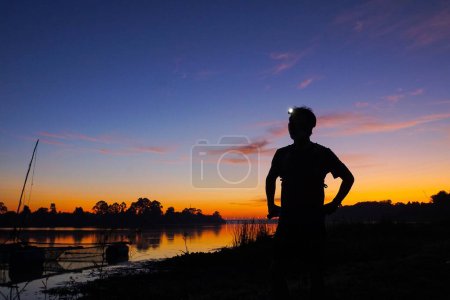 Silhouette of man by river at sunset