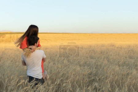 Photo for A young man picked up his woman in his arms and carries her on sunset in wheat field. - Royalty Free Image