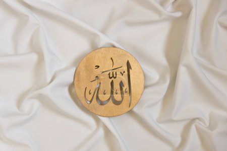 Foto de Nombres de Allah bismillah. Caligrafía dorada de madera del dios islam. sobre textil blanco, vista superior - Imagen libre de derechos