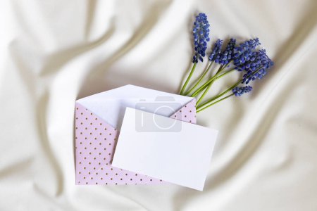 Rosafarbener Umschlag mit leerer Karte und Muscari-Blume auf weißem Hintergrund. Ansicht von oben