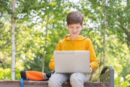 Sonriente adolescente trabajando en el portátil. Sosteniendo y utilizando un ordenador portátil para la creación de redes en un día soleado de primavera, al aire libre