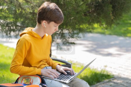 Niño adolescente reflexivo que trabaja en el portátil. Sosteniendo y utilizando un ordenador portátil para la creación de redes en un día soleado de primavera, al aire libre