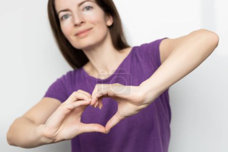Inklusion anregen. Frau hält ihre Hände in Herzform und hält sie vor sich, gekleidet in ein lila T-Shirt. Konzept zum Internationalen Frauentag