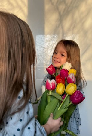 Frères et soeurs ou jumeaux. Fête des femmes ou des mères. Portrait de deux fillettes souriantes avec un bouquet de tulipes. Espace pour le texte