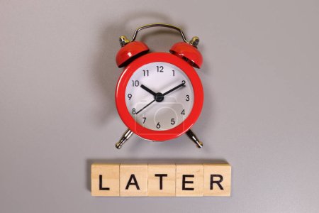 Later word and alarm clock on gray background
