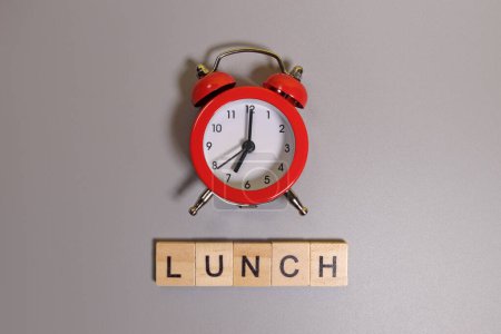 Mittagessen Wort und Wecker auf grauem Hintergrund