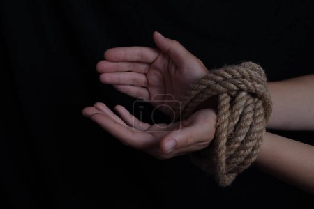 Foto de Manos de niña atadas con una cuerda sobre un fondo negro - Imagen libre de derechos