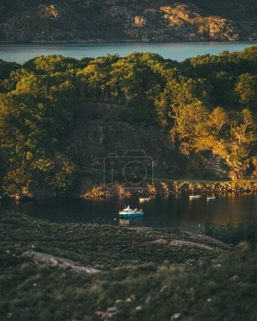 Téléchargez les photos : Image décalée inclinée d'un petit bateau de pêche bleu dans un Loch dans les Highlands écossais pendant l'heure dorée. - en image libre de droit