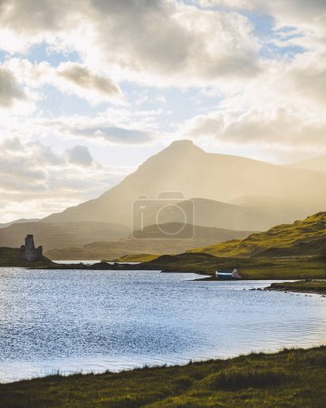 Téléchargez les photos : Brouillard engloutissant une montagne dans les Highlands écossais à côté d'un grand Loch avec un petit château pittoresque sur la rive. - en image libre de droit