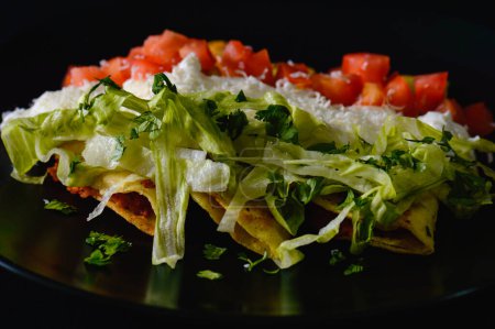 Photo for Mashed potato and chorizo fried tacos dorados with lettuce, tomatoes, sour cream and cotija cheese. Shot on black background. - Royalty Free Image