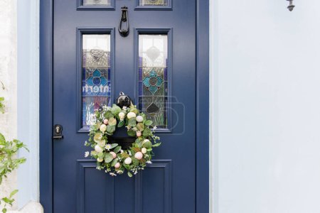 A blue door with a wreath on it. The wreath is made of flowers and is hanging from the door