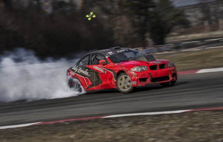 Photo for 12-05-2022 Riga, Latvia a red car with smoke coming out of it's exhaust system on a race track with trees in the background - Royalty Free Image
