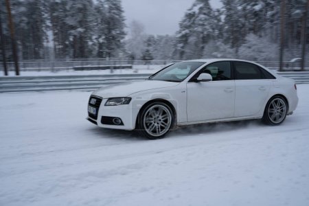 Téléchargez les photos : 12-12-2022 Riga, Lettonie une voiture blanche conduisant sur une route enneigée à côté d'une forêt d'arbres et une clôture dans la région. . - en image libre de droit
