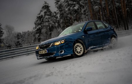 Téléchargez les photos : 12-12-2022 Riga, Lettonie une voiture bleue conduisant sur une route enneigée à côté d'une forêt d'arbres et une clôture avec de la neige dessus. . - en image libre de droit