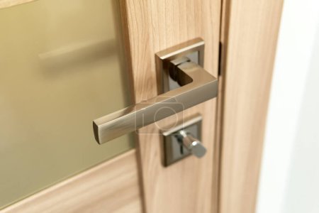 Photo for Close-up of a modern chrome metal door handle on wooden door. - Royalty Free Image