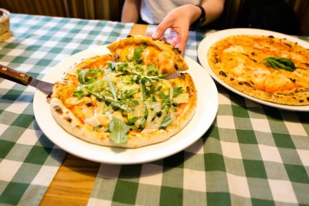 Photo for Female hands taking slices of authentic Italian caesar stone oven pizza with arugula, sauce, grilled chicken, herbs and spicy parmesan cheese. High quality photo. - Royalty Free Image
