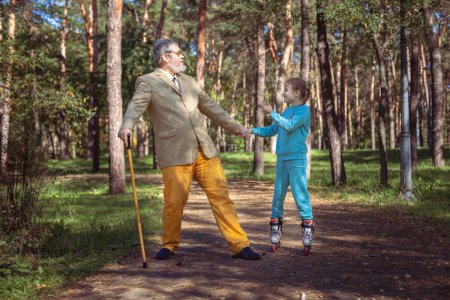 Photo for Grandfather walks with his granddaughter in the park. A girl roller skates in the park with her old grandfather. A funny grandfather and a little girl are playing and joking. - Royalty Free Image