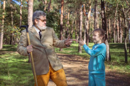 Foto de El abuelo camina con su nieta en el parque. Un abuelo divertido y una niña están jugando y bromeando. - Imagen libre de derechos