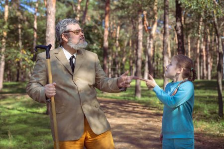 Photo for Grandfather walks with his granddaughter in the park. A funny grandfather and a little girl are playing and joking. - Royalty Free Image