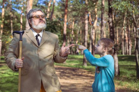 Téléchargez les photos : Grand-père marche avec sa petite-fille dans le parc. Un grand-père drôle et une petite fille jouent et plaisantent. - en image libre de droit