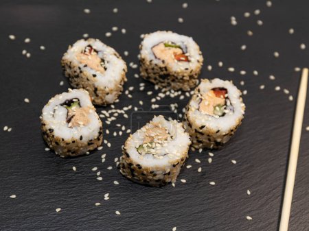 Sushi futomaki z surimi, marchewką, pieprzem i roztopionym serem na czarnej kamiennej płycie