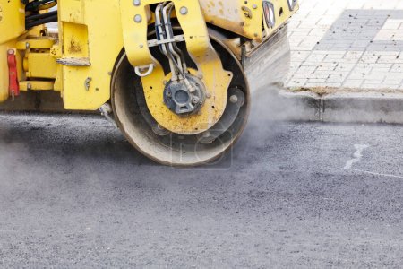 Rouleau de route et machine de pavage d'asphalte sur le chantier, avec du béton chaud et de la fumée
