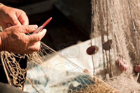 Téléchargez les photos : Filet de pêche dans les mains du pêcheur, il tisse et répare en cousant les filets avec une aiguille et un fil - en image libre de droit